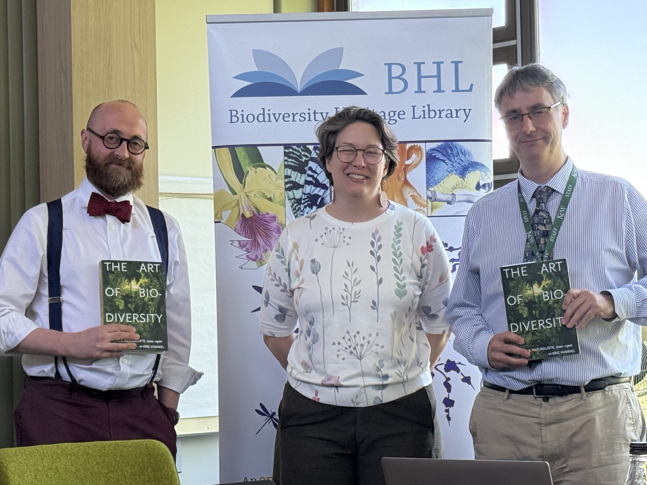 Three smiling people standing in front of a Biodiversity Heritage Library banner, two holding books "The Art of Biodiversity".