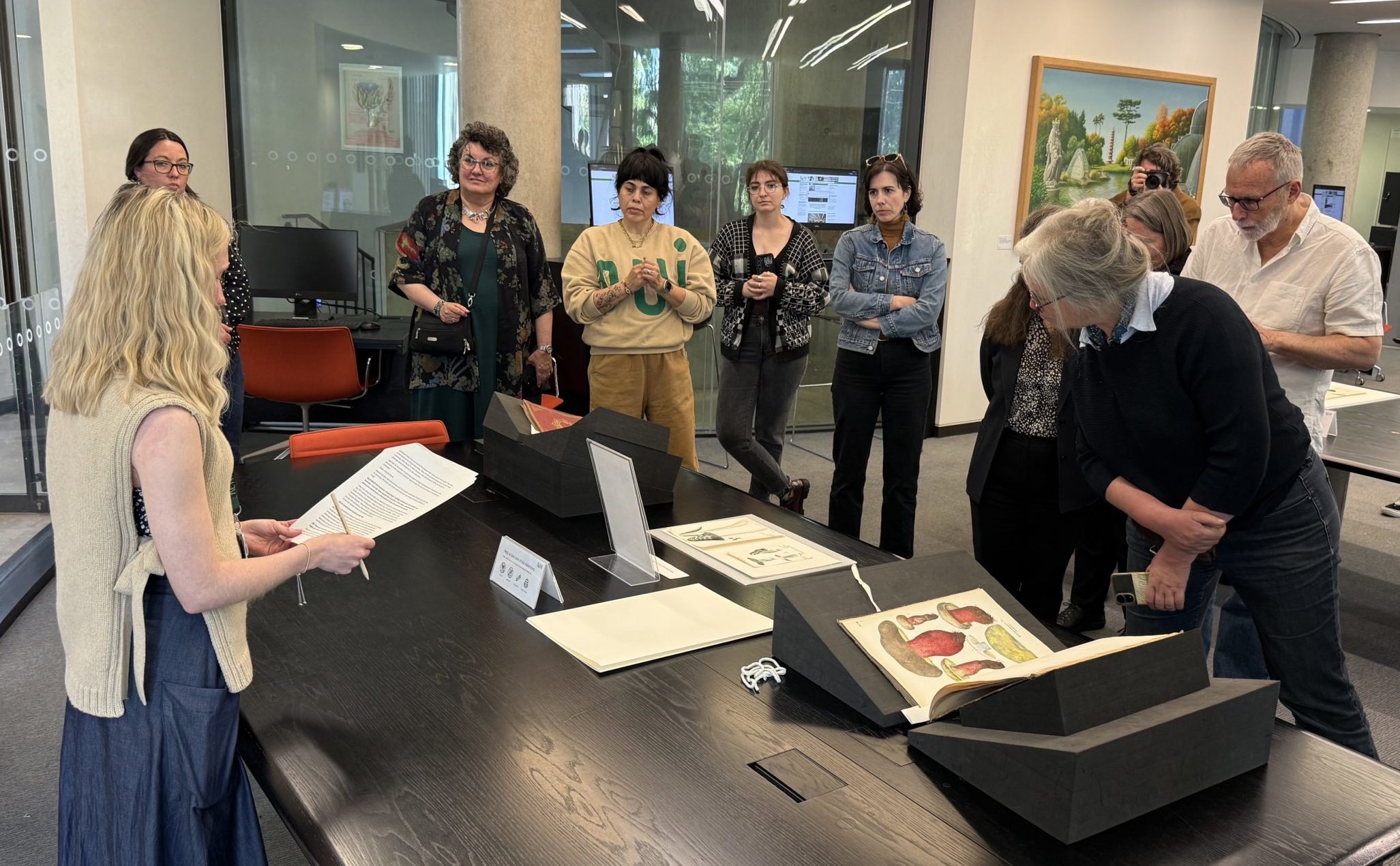 A group of people standing around a table covered in books in a library.