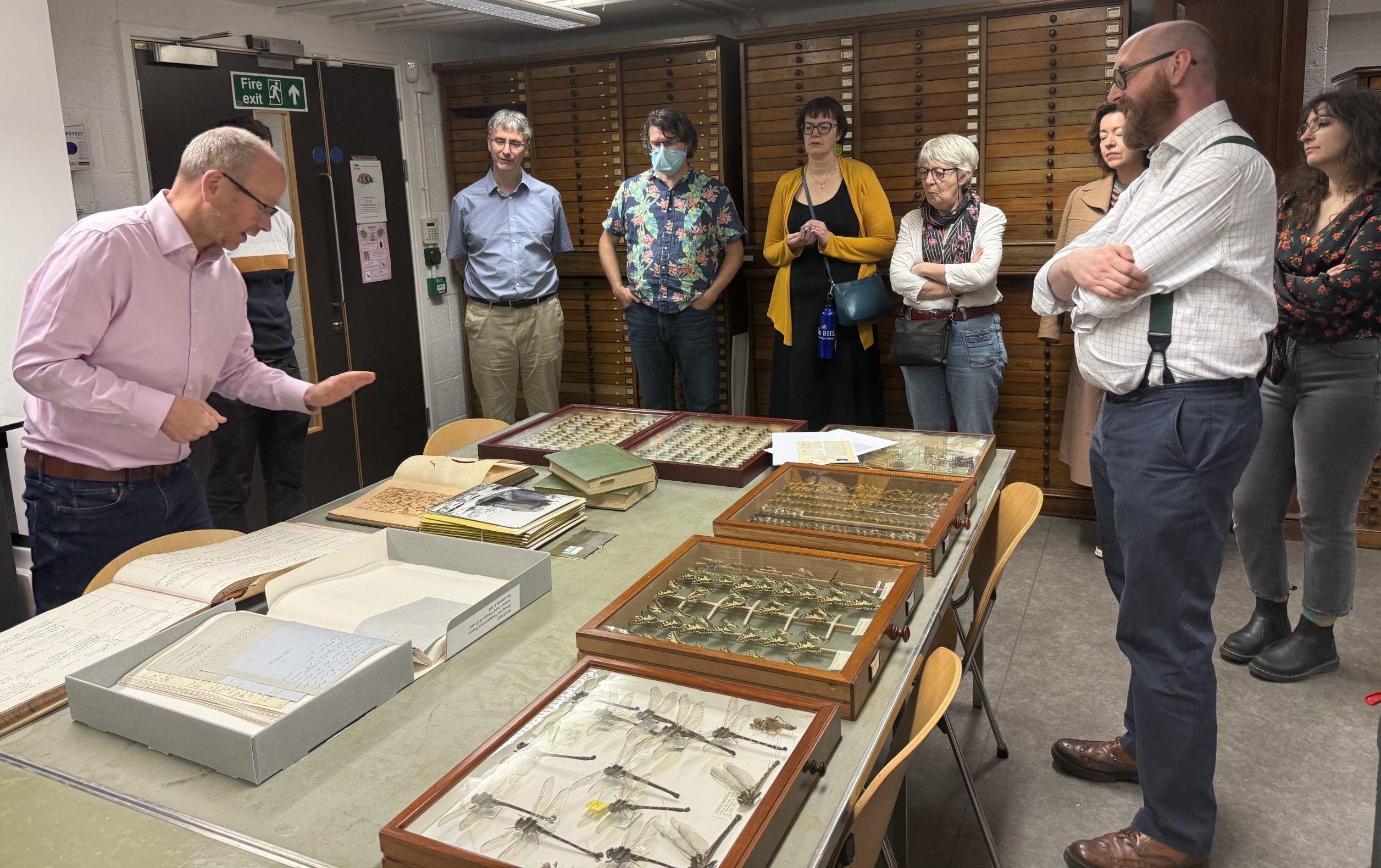 A group of people standing around a table covered in insect specimens, books, and archival material.
