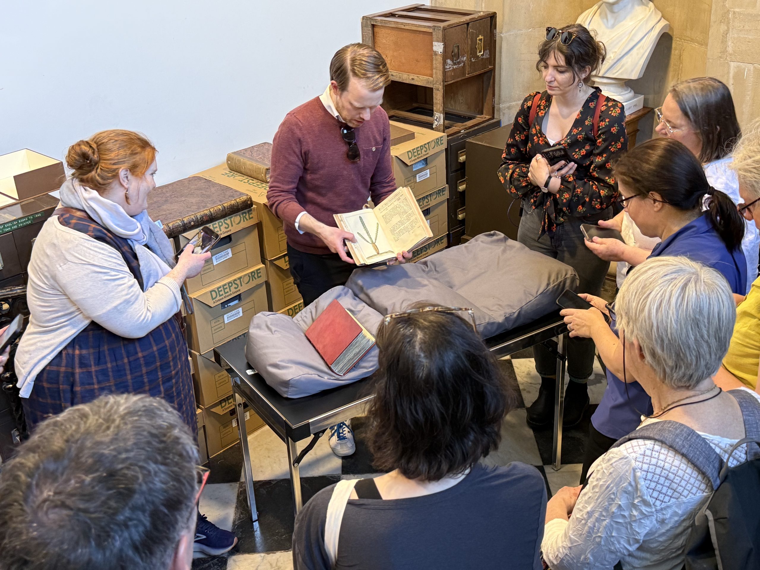 A group of people standing around a table looking at a man holding an open book.