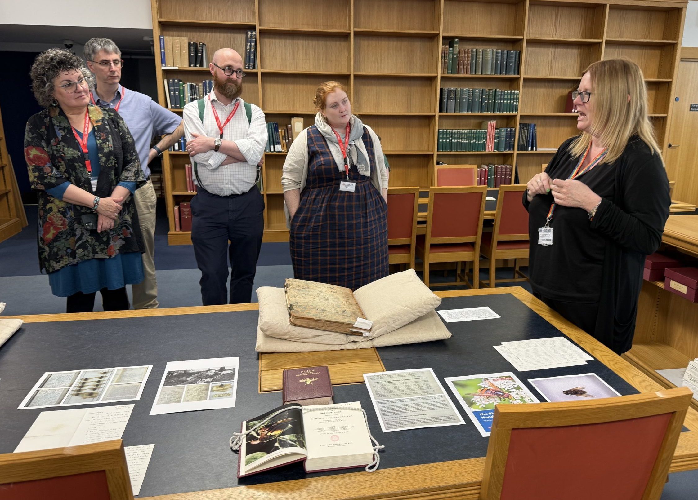 A group of people standing around a table covered in books and brochures in a library.